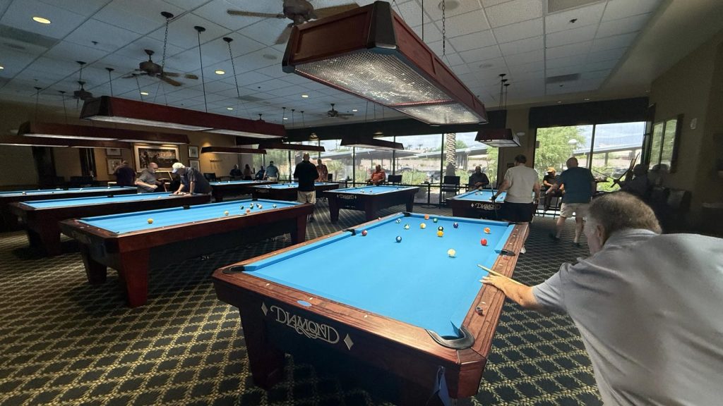 A member takes a shot while others play at tables across the hall