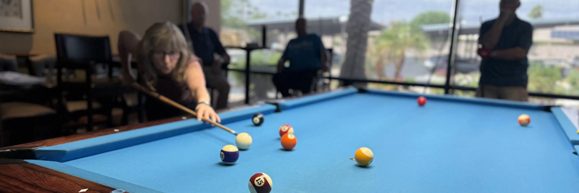 A member lines up a shot on a blue-cloth pool table by the hall windows